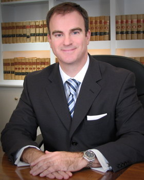 Phillip J. Collins in a dark suit and tie at his desk in front of a wall of legal books.